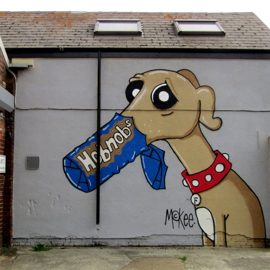 Dog with it's mouth in a Hobnob's packet, painted on the side of a building in Kelham Island by Pete McKee